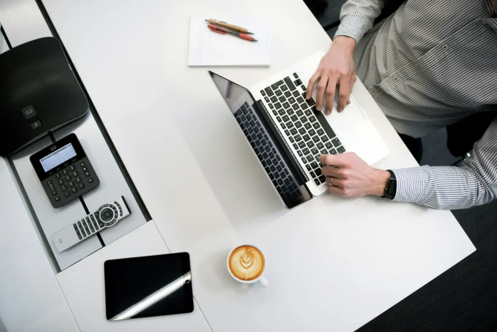 Imagem de um profissional trabalhando em modelagem financeira para negócios digitais, usando laptop em ambiente de escritório com caderno, canetas e smartphone