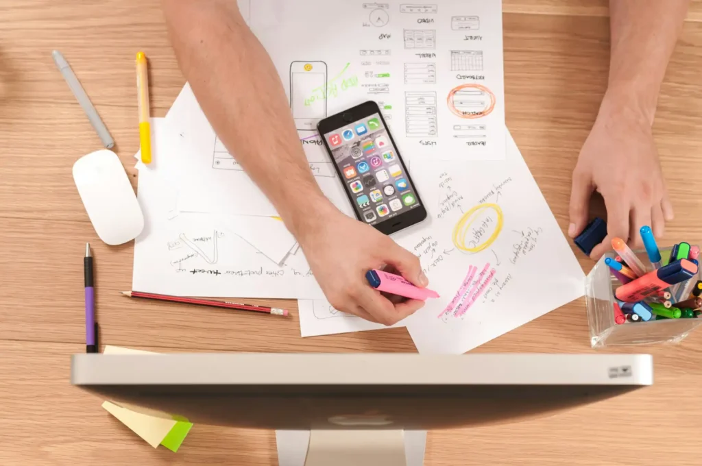 Pessoa planejando sua trajetória profissional usando análise SWOT pessoal, com materiais de escritório, smartphone e anotações em uma mesa de trabalho.