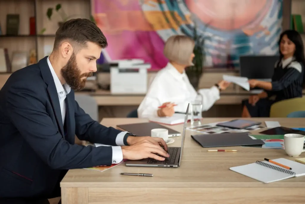 Profissional focado em planejamento de carreira, estudando estratégias de sucesso do estágio ao cargo executivo, em ambiente de escritório, com colegas ao fundo.