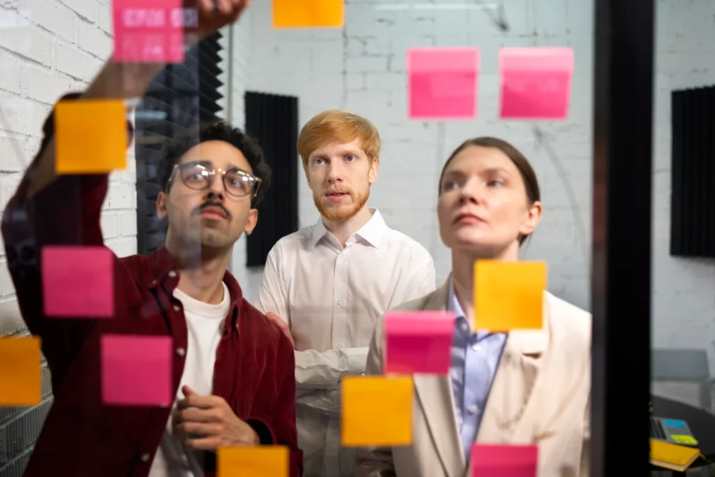 Três profissionais discutindo habilidades sociais valorizadas por recrutadores em 2025 durante uma reunião com post-its coloridos na parede, simbolizando soft skills importantes.